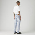 A person in a plain white T-shirt and Levi's 555 Relaxed Straight vintage-inspired jeans, crafted from recycled water, stands facing away against a gray background.