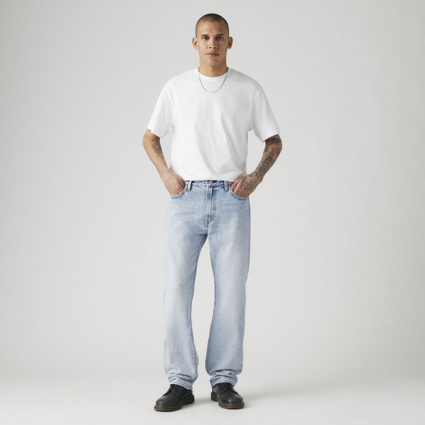 A person stands against a neutral background, wearing a white T-shirt, Levis 555 Relaxed Straight jeans crafted from vintage-inspired non-stretch denim, and black shoes.