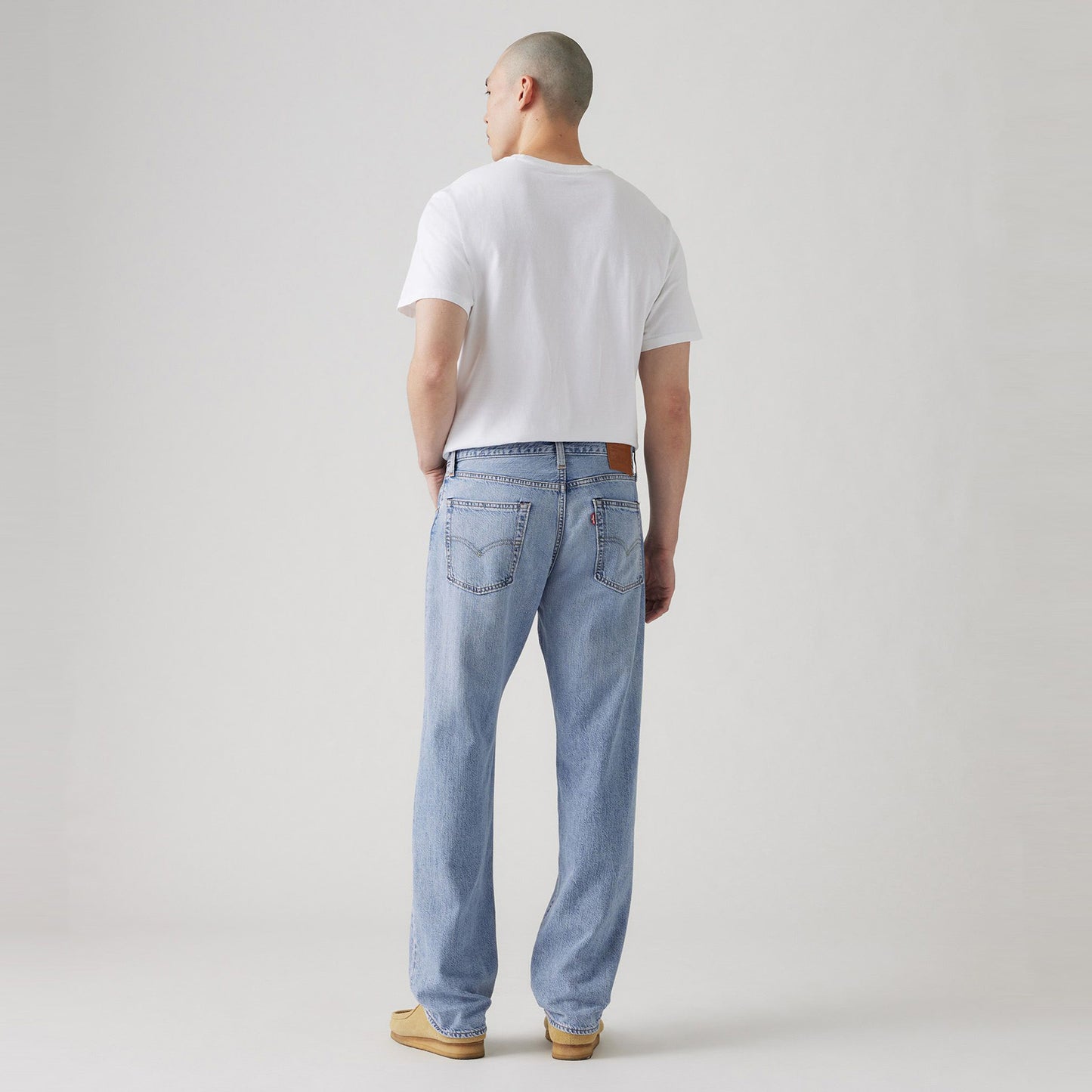 A person stands facing away against a plain background, wearing a white t-shirt, Levis 555 Relaxed Straight vintage-inspired blue jeans, and brown shoes.