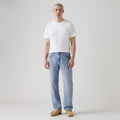 Against a plain background, someone wears a white t-shirt, Levis 555 Relaxed Straight jeans with a vintage-inspired style, and brown shoes.