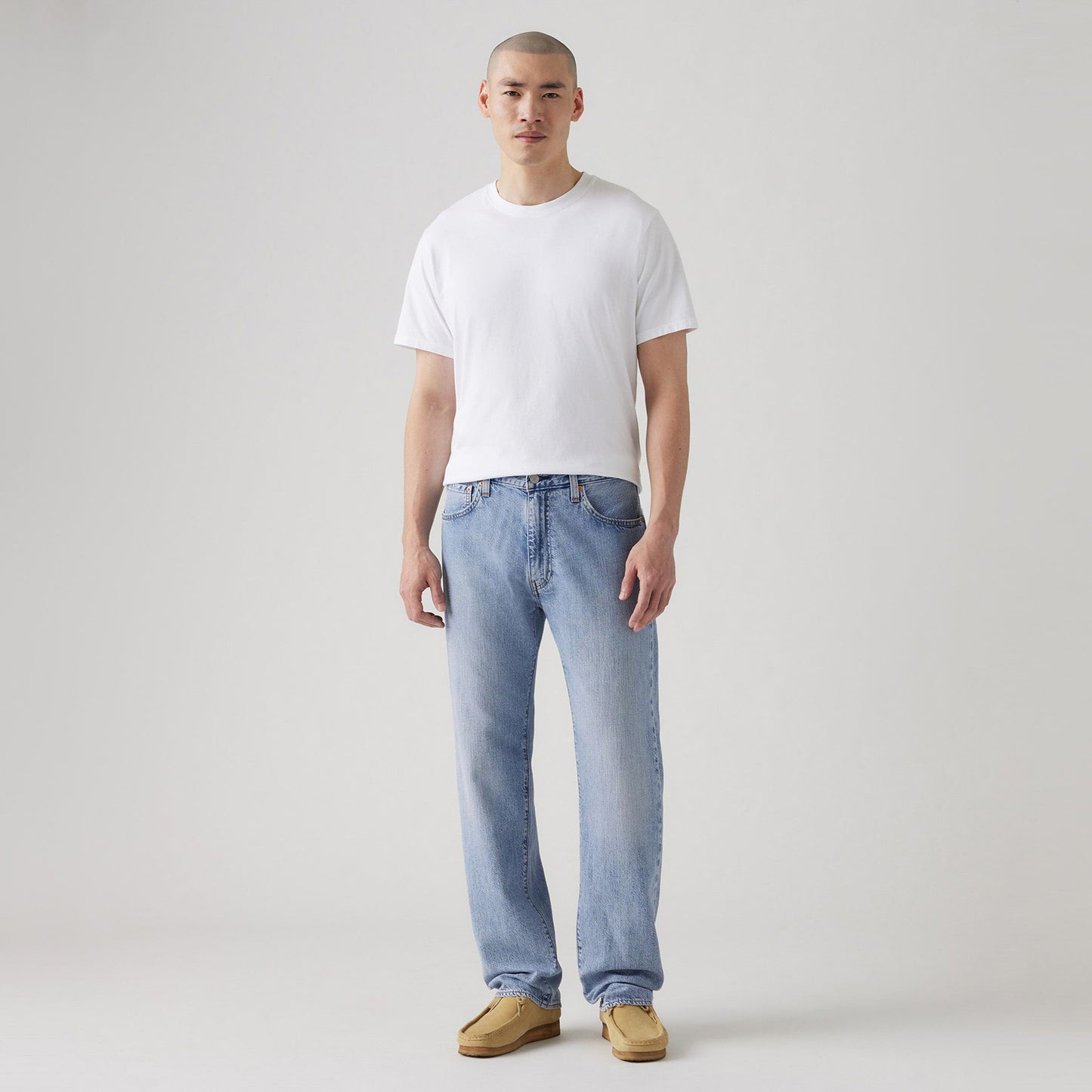 Against a plain background, someone wears a white t-shirt, Levis 555 Relaxed Straight jeans with a vintage-inspired style, and brown shoes.