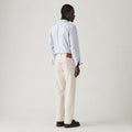 A person wearing Levis' 501 Original, Rent Free LTWT—a light blue striped shirt with cream straight-fit pants—stands facing away against a plain background, completing the outfit with dark shoes.