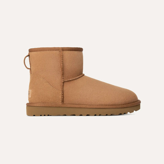 The W Classic Mini II by Ugg is a tan suede ankle boot featuring a flat rubber sole, distinctive stitching details, and a convenient back pull tab, embodying West Coast cool.