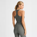 A person in the Ribbed R Tank by Rohnisch, featuring a sleek racerback design and gray athletic wear, stands sideways against a plain background.