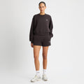 A person wears the Rohnisch Soft Sweatshirt, black and cropped with logo embroidery, paired with shorts, white socks, and silver sneakers against a plain background.