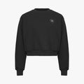 The Soft Sweatshirt by Rohnisch is a black cropped design with long sleeves, made from recycled fabric. It showcases the brand's signature white logo embroidery on the upper left chest.