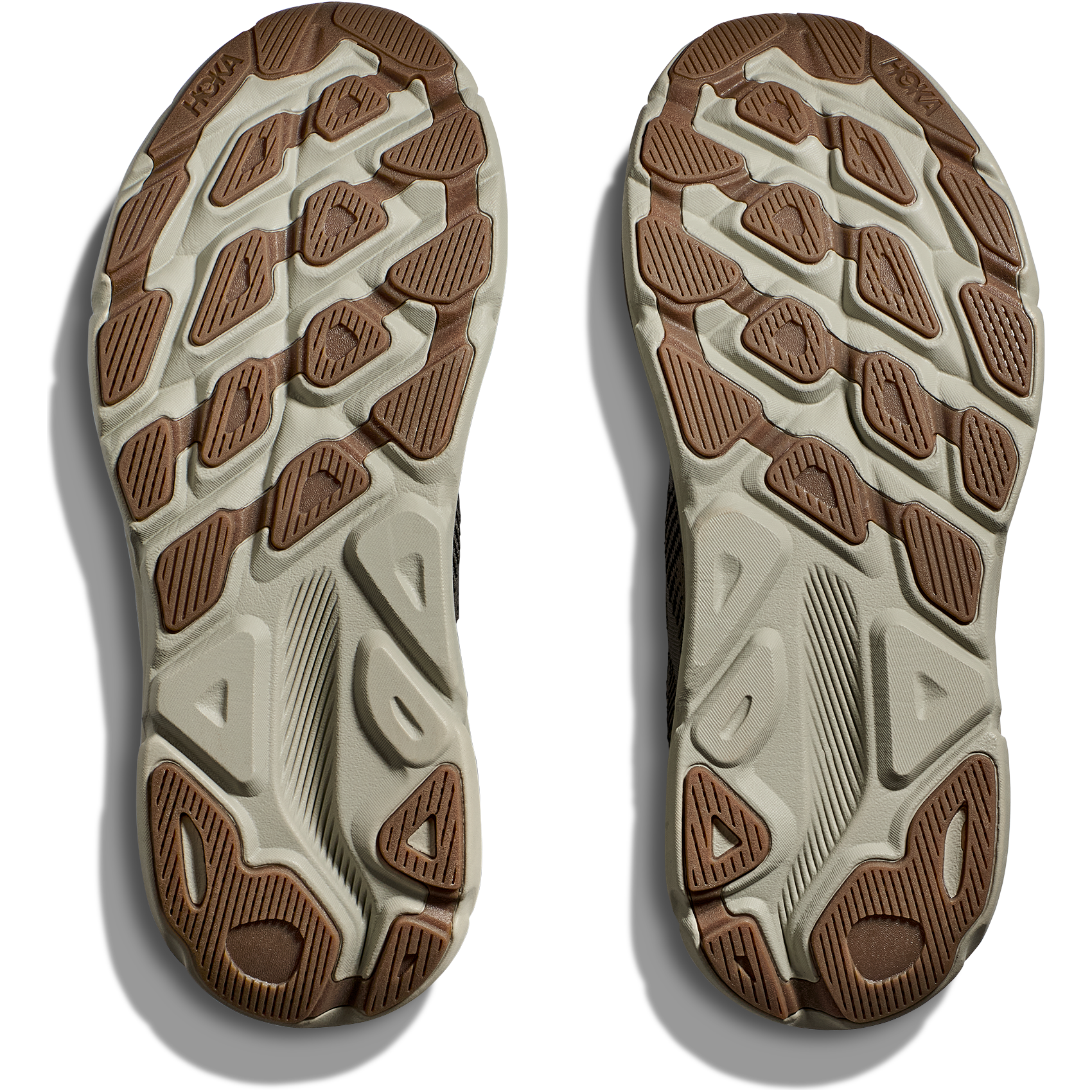 The image shows the soles of a pair of Hoka M Clifton 9, Black/Slate athletic shoes, featuring a textured tread pattern with brown and beige sections designed for responsive toe-off.