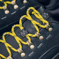 Close-up of the Hoka U Tor Summit, Black hiking boot featuring bright yellow laces threaded through silver hooks and metal eyelets.