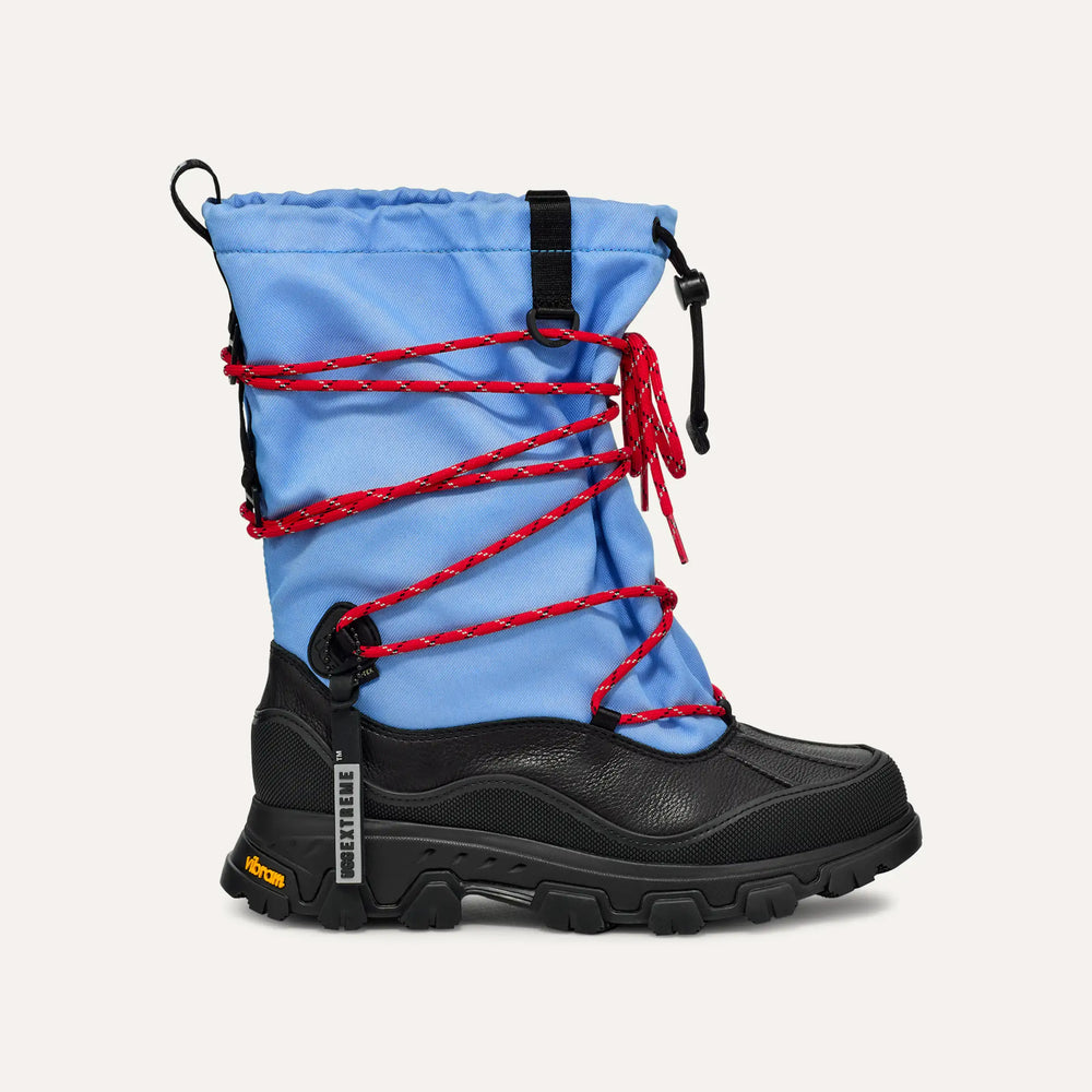 The W Metropeak by Ugg is a stylish winter boot with a waterproof design, black sole and toe, light blue upper, and distinctive red rope lacing in a crisscross pattern.