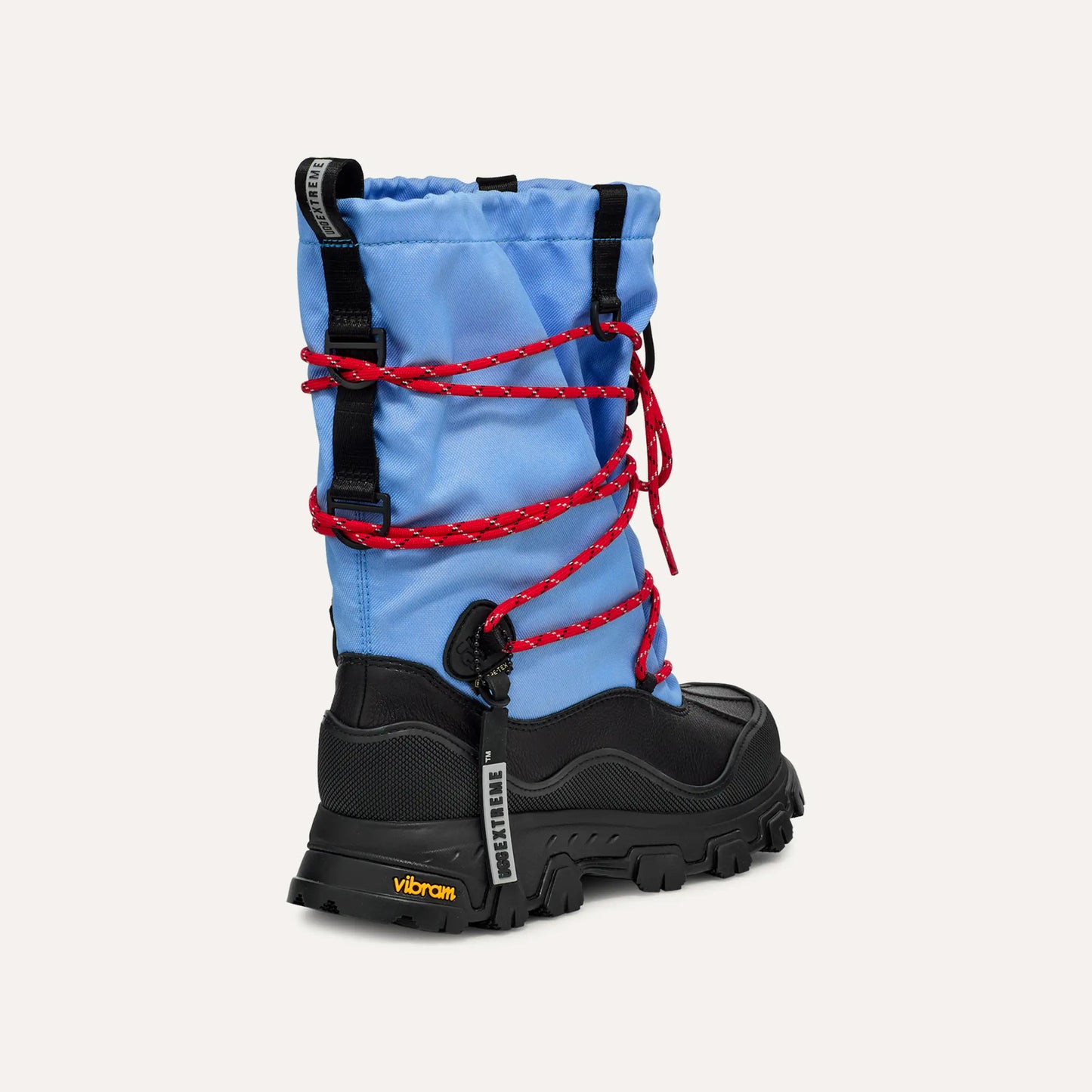 The Ugg W Metropeak Boot features a blue and black waterproof design, red laces, Vibram sole, and a tall insulated upper for warmth and comfort in harsh conditions.