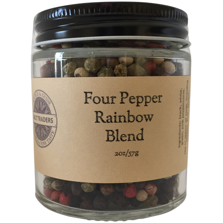 A glass jar labeled "Salt Traders Four Pepper Blend - Rainbow Pepper" brimming with mixed black, white, green, and red peppercorns to season foods.