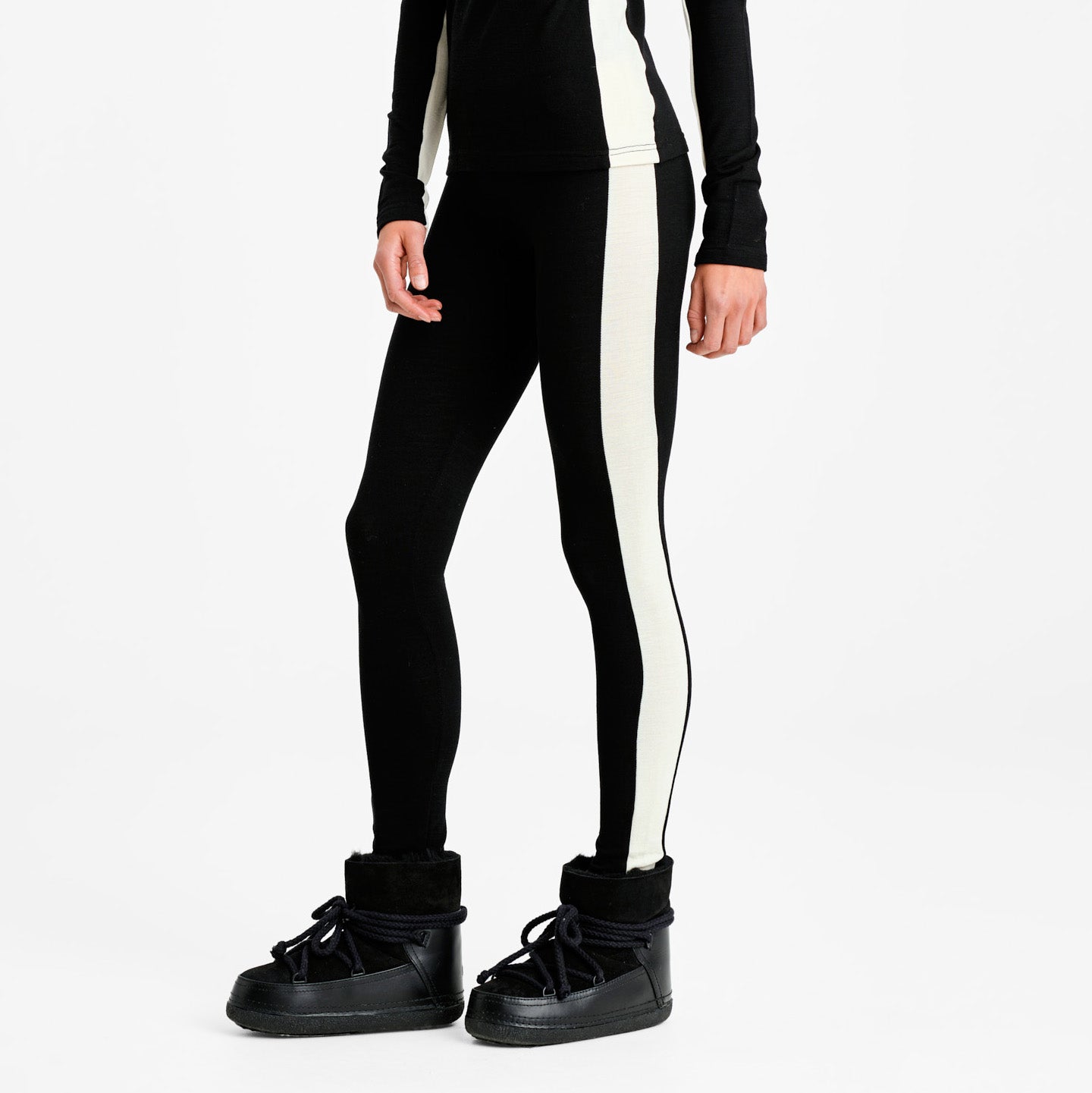 The individual is wearing black W Voss Leggings from We Norwegians, made of premium Merino wool with a chic white stripe. Paired with sleek boots, these women's leggings provide unmatched comfort and style.