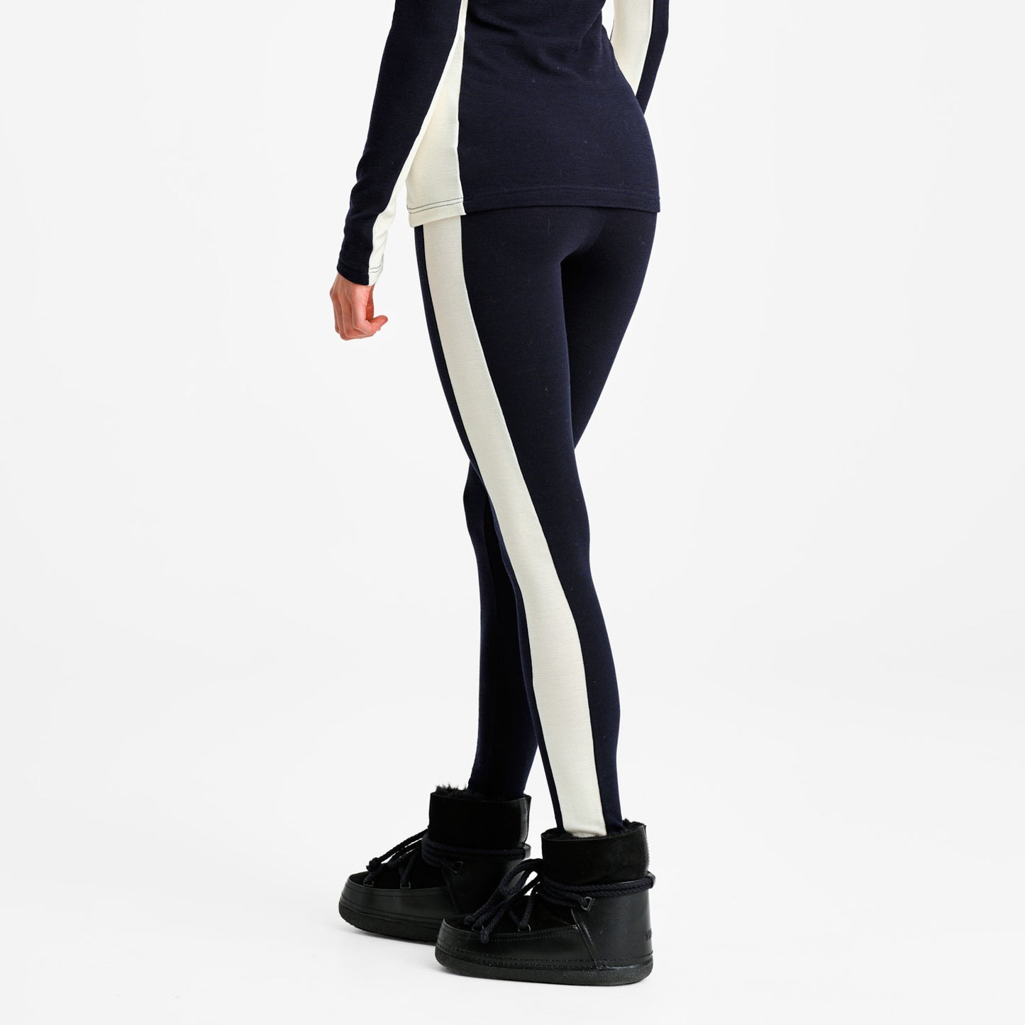 A person is shown from the back wearing We Norwegians W Voss Leggings—black with white side stripes—and black ankle boots against a plain background. These elegant leggings, designed in women's sizing, provide comfort and style for any occasion.