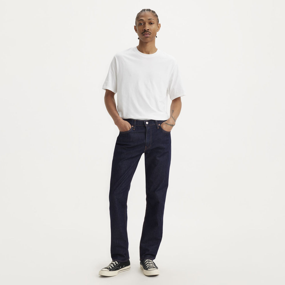 A person stands against a white background wearing Levis' 541 Athletic Taper in Mid Knight Rinse ADV, paired with a white T-shirt and black sneakers. This outfit highlights an athletic build enhanced by advanced stretch technology for ultimate comfort.