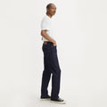 A model in a white t-shirt, dark jeans, and black sneakers showcases the comfort and flexibility of Advanced Stretch Technology in Levis' 541 Athletic Taper, Mid Knight Rinse ADV—ideal for athletic builds. Standing sideways with hands in pockets against a white backdrop, it exudes style.