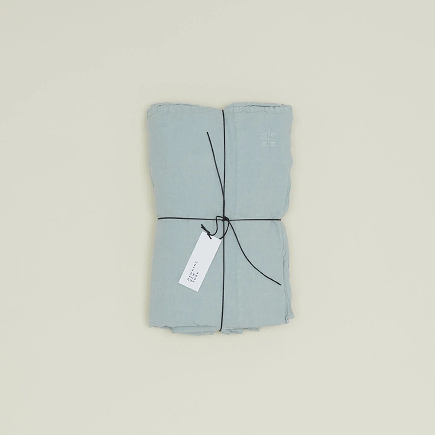 The Simple Linen Fitted Sheet - Queen by Hawkins New York is a stonewashed light blue fabric, crafted in Portugal, elegantly tied with a black string and features a small white tag.