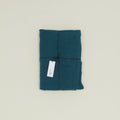 A neatly folded Simple Linen Fitted Sheet - Queen by Hawkins New York, stonewashed in teal and tied with a black string, features a white tag attached.