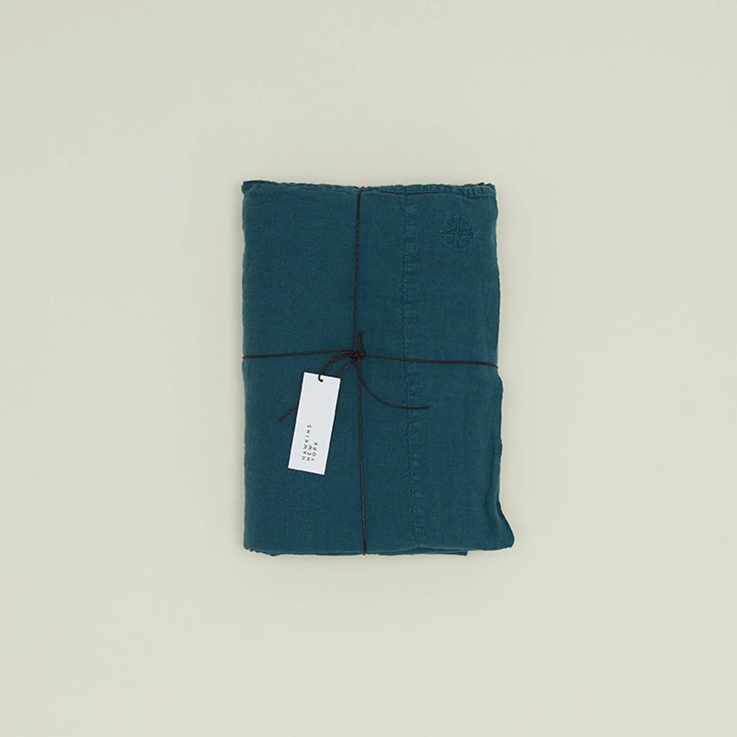 A neatly folded Simple Linen Fitted Sheet - Queen by Hawkins New York, stonewashed in teal and tied with a black string, features a white tag attached.