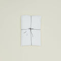 The Simple Linen Fitted Sheet - Queen by Hawkins New York, neatly folded and tied with black string featuring a white tag, graces a plain cream background.