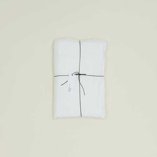 The Simple Linen Fitted Sheet - Queen by Hawkins New York, neatly folded and tied with black string featuring a white tag, graces a plain cream background.