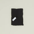 A folded black fabric bundle, crafted from European linen and tied with string, features a small white tag hinting at its origins. It's the Simple Linen Fitted Sheet - Queen by Hawkins New York, woven in Portugal.