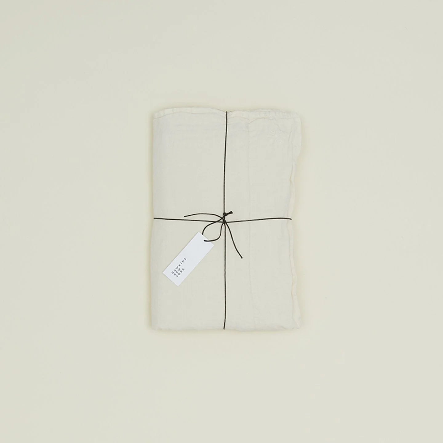 A neatly folded white fabric from Hawkins New York, woven in Portugal, tied with a black string and tagged, showcases the European stonewashed softness of the Simple Linen Fitted Sheet - Queen against a light background.