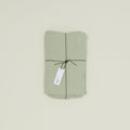 The Simple Linen Fitted Sheet in a light green shade, woven in Portugal by Hawkins New York, is folded and tied with black string and a white tag, displayed on a plain background.