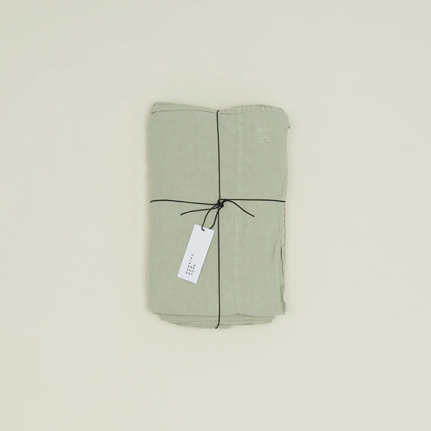 The Simple Linen Fitted Sheet in a light green shade, woven in Portugal by Hawkins New York, is folded and tied with black string and a white tag, displayed on a plain background.