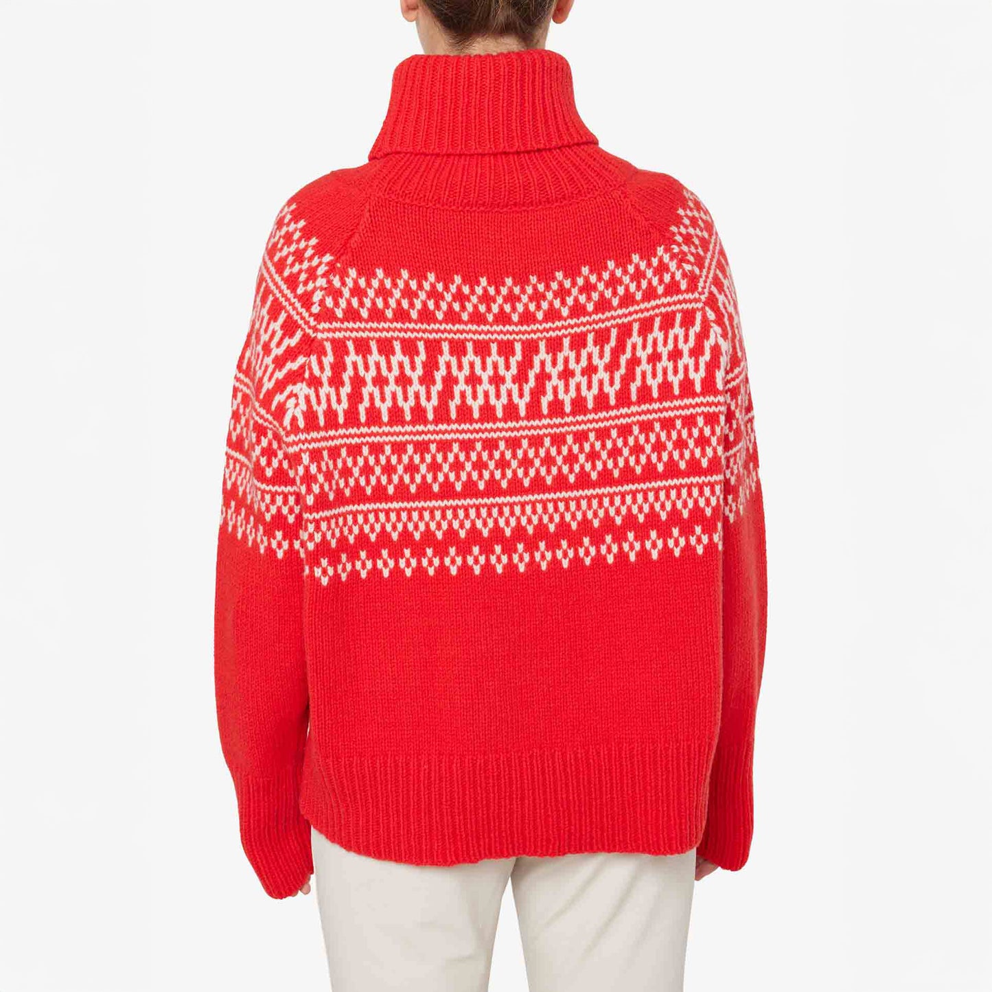 A person is shown from the back wearing the W Setesdal Sweater by We Norwegians, a red turtleneck with white geometric patterns paired with white pants. Made from extra fine merino wool, it showcases elegance and quality.