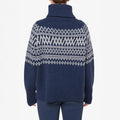 A person is seen from the back wearing a W Setesdal Sweater by We Norwegians. It features a dark blue turtleneck with white geometric patterns, hinting at luxurious cashmere construction, adding sophistication to the stylish ensemble.