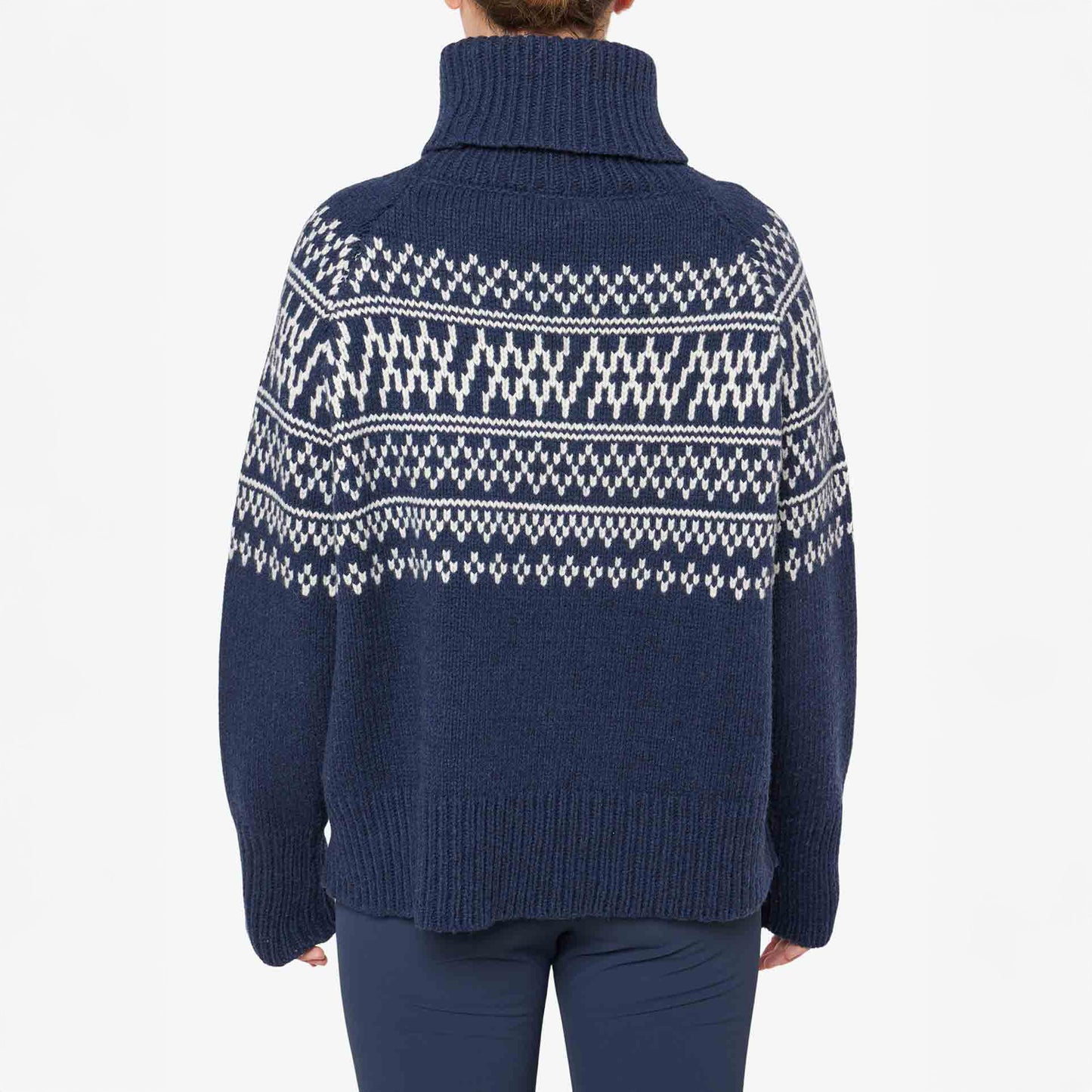 A person is seen from the back wearing a W Setesdal Sweater by We Norwegians. It features a dark blue turtleneck with white geometric patterns, hinting at luxurious cashmere construction, adding sophistication to the stylish ensemble.