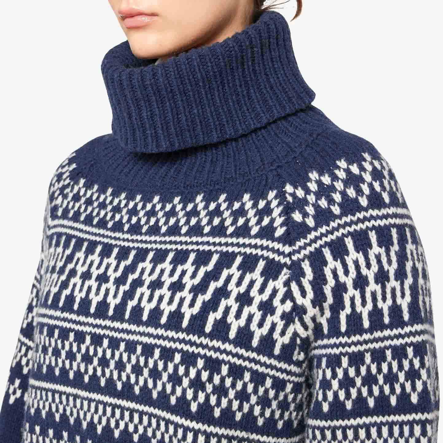 The individual is elegantly dressed in a W Setesdal Sweater by We Norwegians, featuring a navy and white pattern. Crafted from soft Merino wool, it ensures both warmth and style.