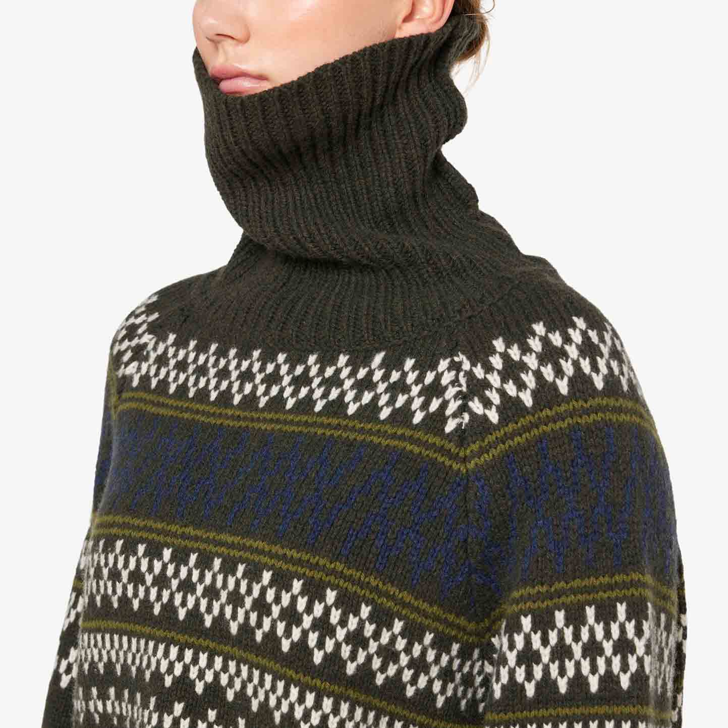 A person wearing the W Setesdal Sweater by We Norwegians, a dark green turtleneck made from extra fine Merino wool, showcases elegant white and blue patterns.