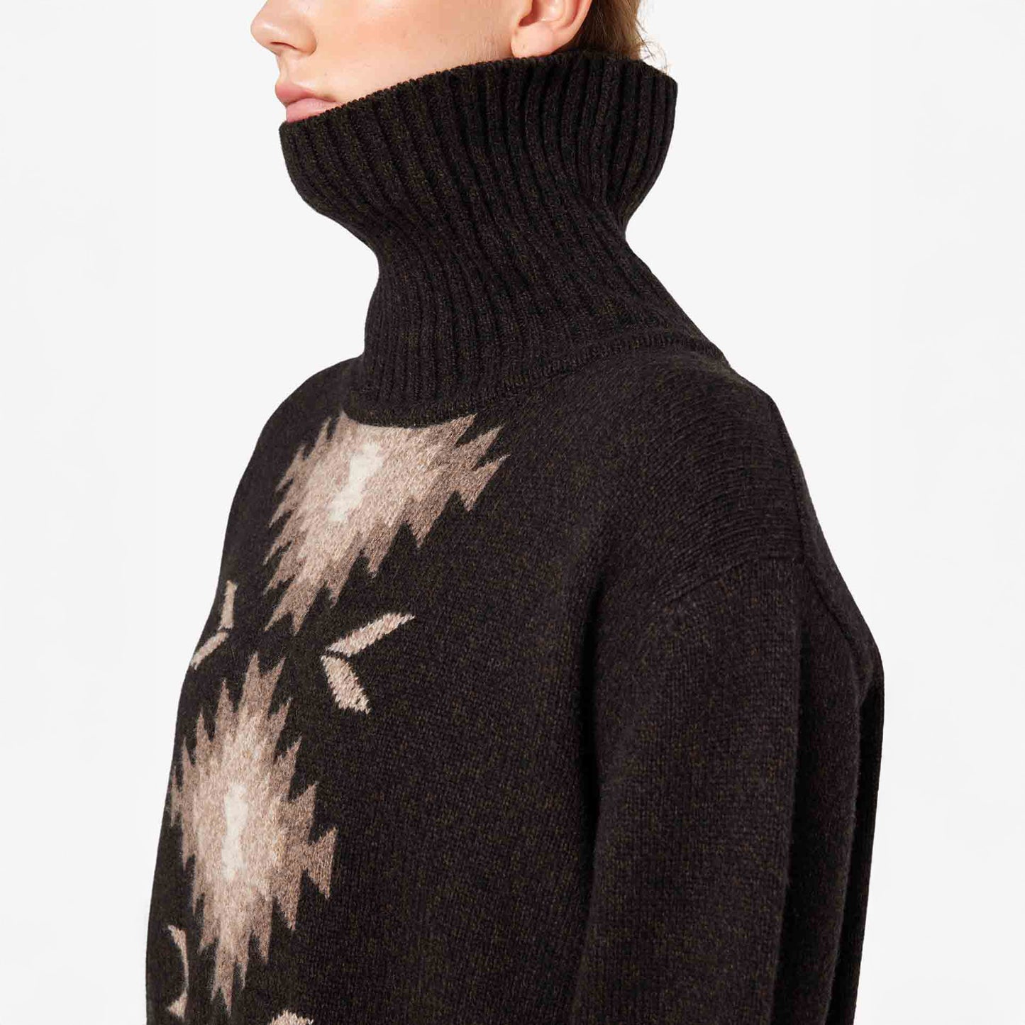 A person is wearing the W Hovden Sweater from We Norwegians, a black high-neck design with a beige geometric pattern, crafted in soft lamb's wool for warmth and style. Available in women's sizes.