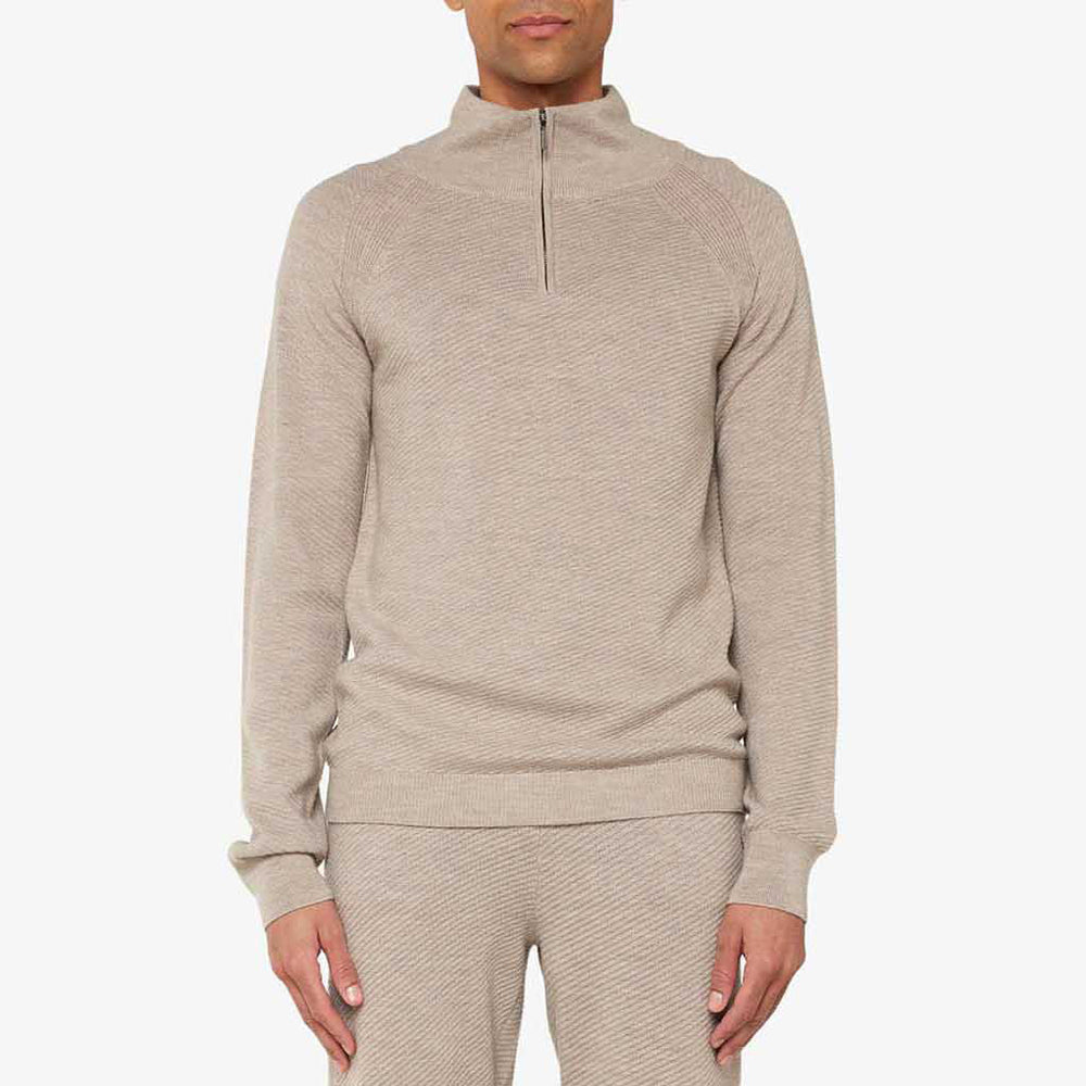 A person is clad in the beige M Geilo 1/4 Zip sweater and matching pants against a plain background. Made from soft merino wool, this attire by We Norwegians enhances its appeal and is thoughtfully designed for men.