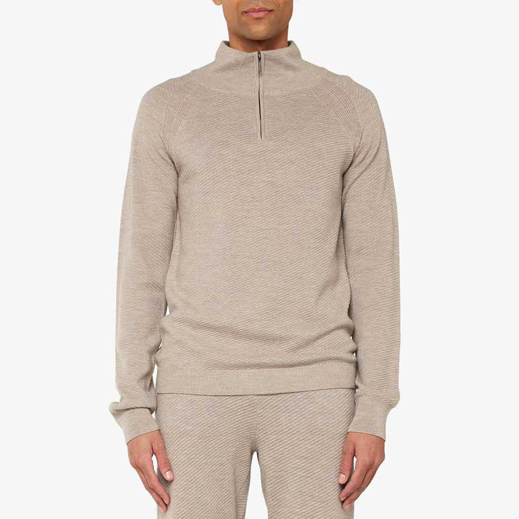 A person is clad in the beige M Geilo 1/4 Zip sweater and matching pants against a plain background. Made from soft merino wool, this attire by We Norwegians enhances its appeal and is thoughtfully designed for men.