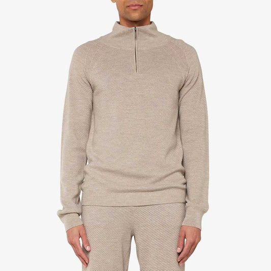 A person is clad in the beige M Geilo 1/4 Zip sweater and matching pants against a plain background. Made from soft merino wool, this attire by We Norwegians enhances its appeal and is thoughtfully designed for men.