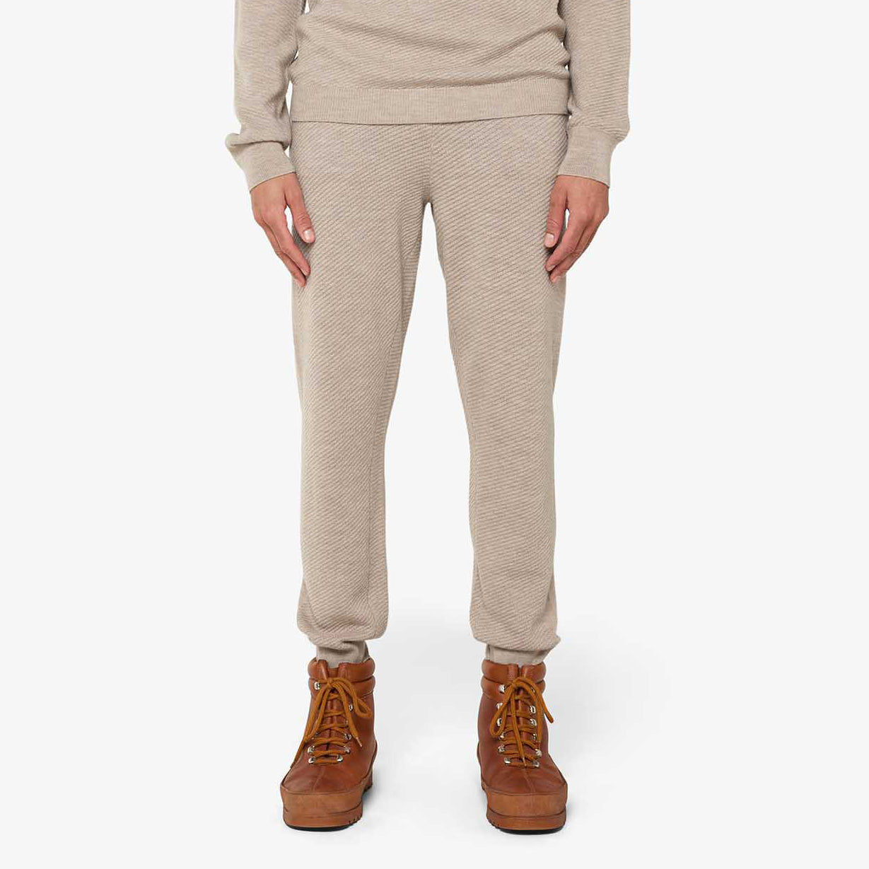 Person wearing M Geilo Jogger, designed by We Norwegians, in light beige with a matching top and brown boots, crafted from fine Merino wool.