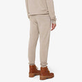 A person wearing the M Geilo Jogger by We Norwegians, a beige tracksuit made of fine Merino wool, and brown boots stands with their back turned.