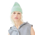 A person wearing a light green Le Bonnet beanie and a gray sleeveless hoodie gazes neutrally at the camera.