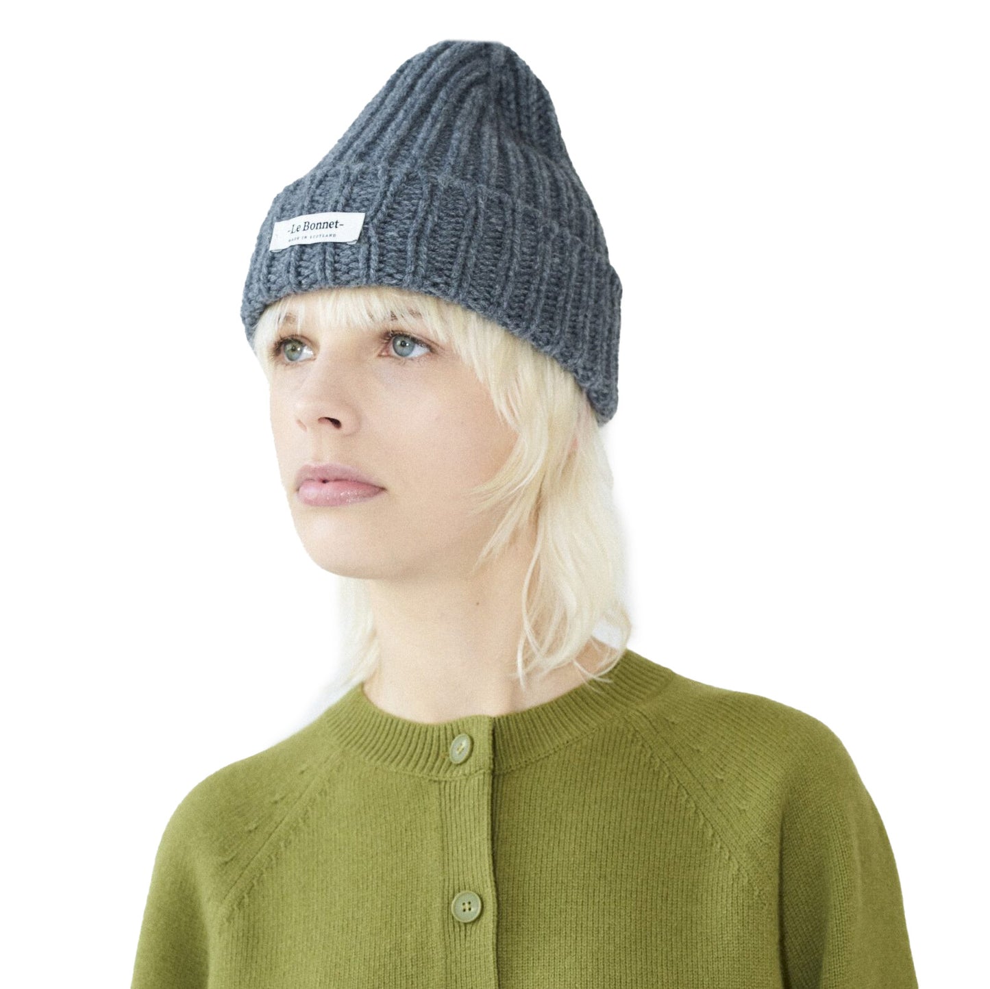 Against a plain background, someone wears a durable Logo Beanie by Le Bonnet in gray, paired with a green button-up shirt.