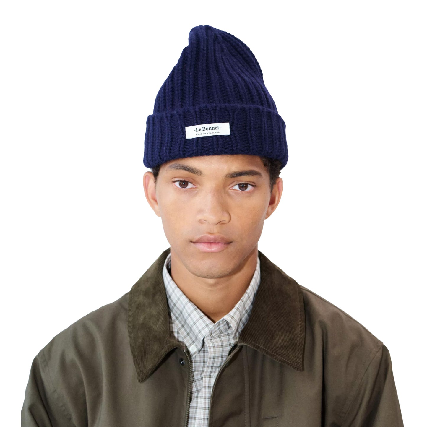 A person wearing a Le Bonnet navy Logo Beanie and a brown jacket over a plaid shirt stands against a white background.