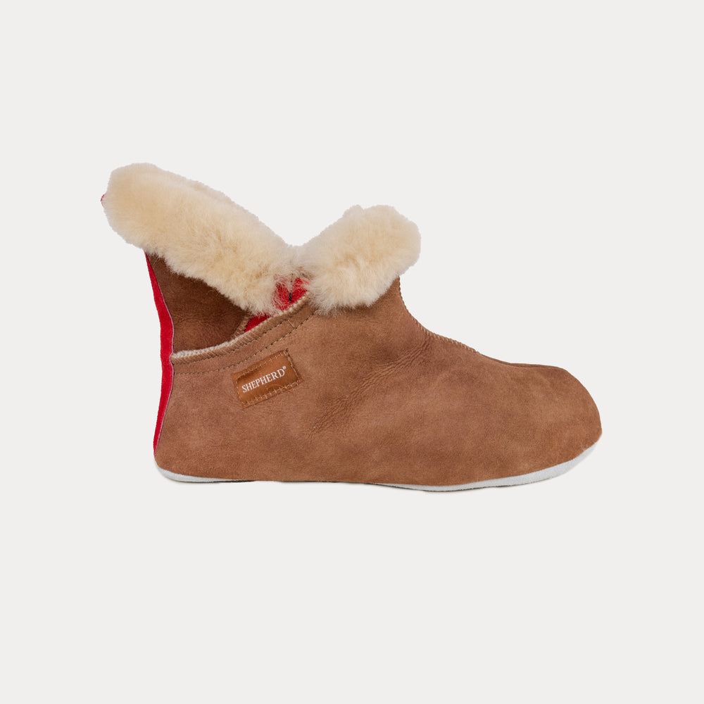 The Emmy Slipper by Shepherd of Sweden in Moro/Chestnut is a brown suede slipper featuring a fluffy cream lining, red heel accent, and side brand label.