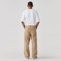 Facing away from the camera, a person wears a white T-shirt paired with Levis' 568 Loose STRT Carpenter beige cargo pants and black shoes, set against a simple background.