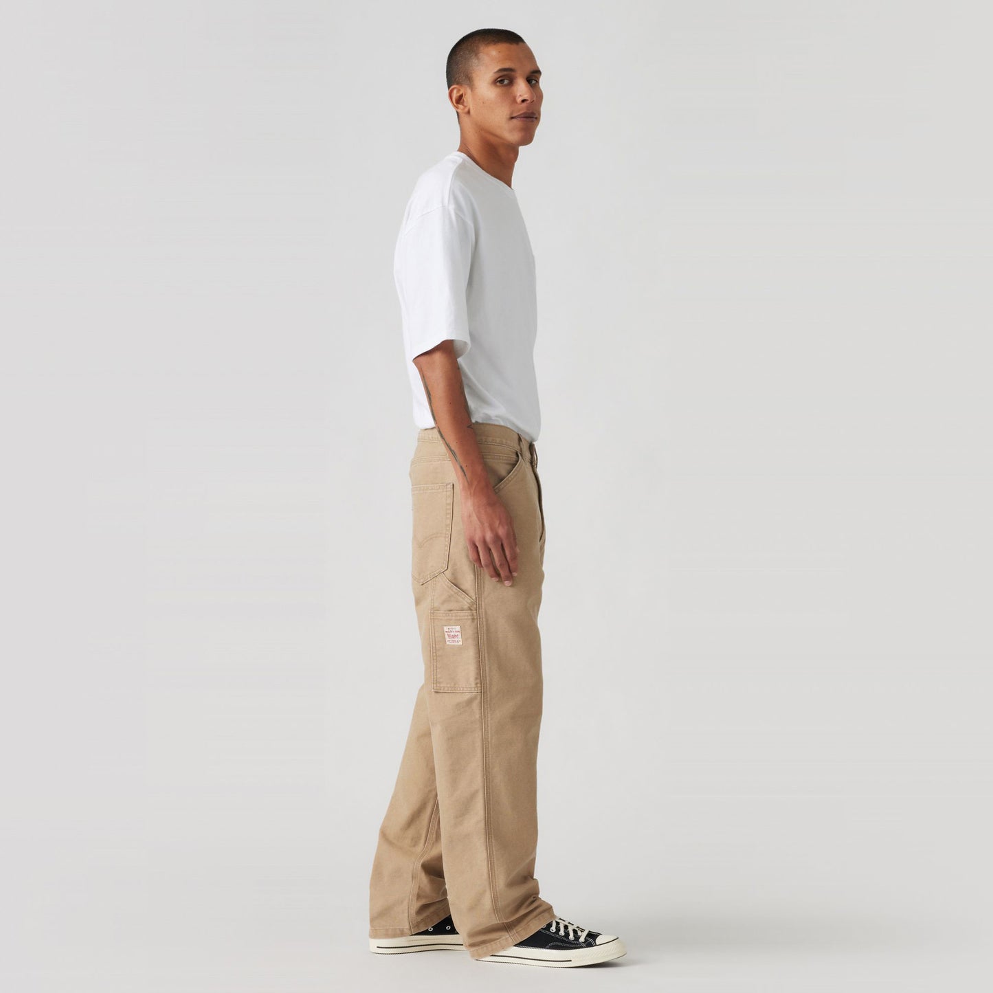 A person in a white T-shirt and Levis 568 Loose STRT Carpenter beige pants stands sideways against a plain background.