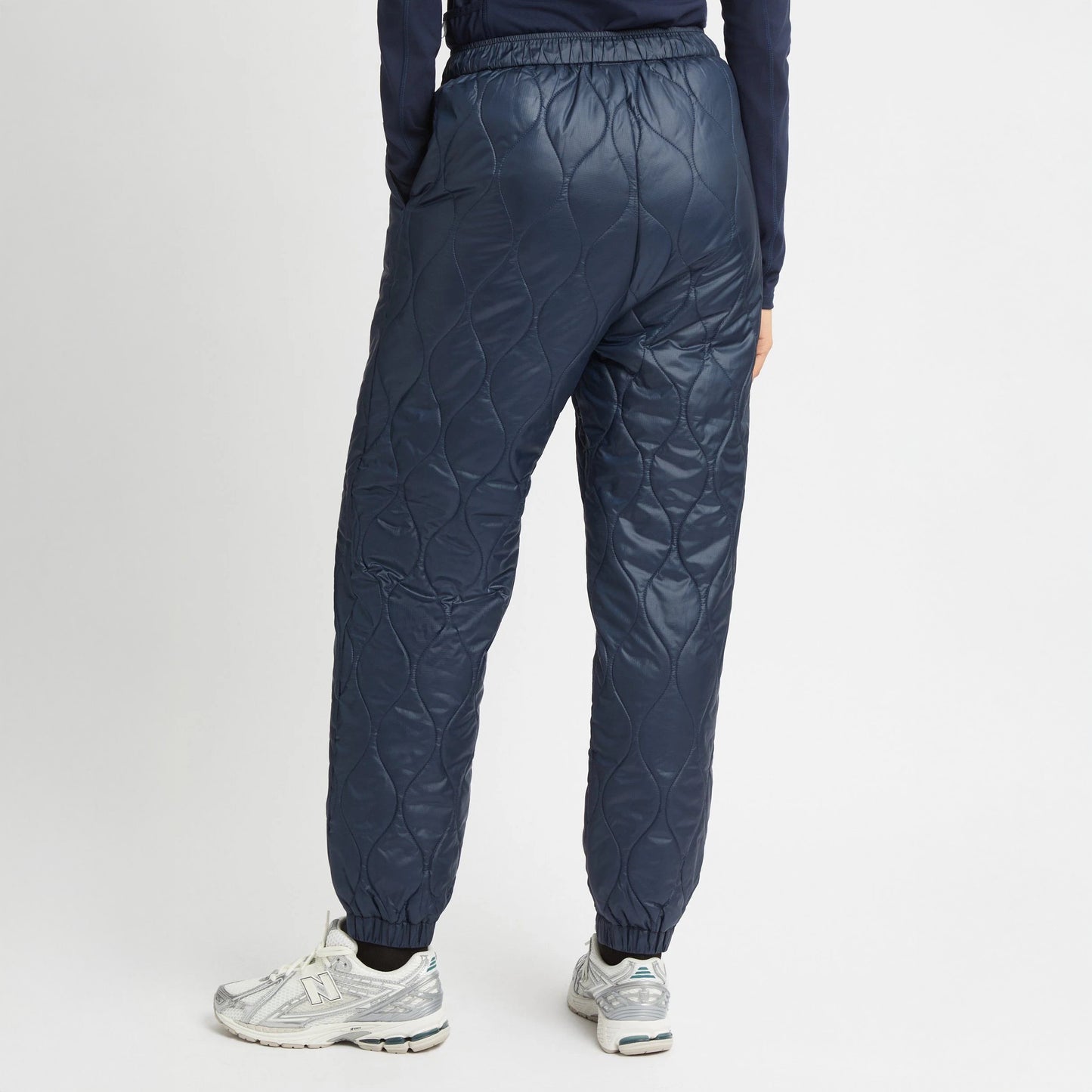 A person wearing Rohnisch's Relaxed Quilt Pants made from recycled ripstop polyester and silver sneakers is seen from behind.