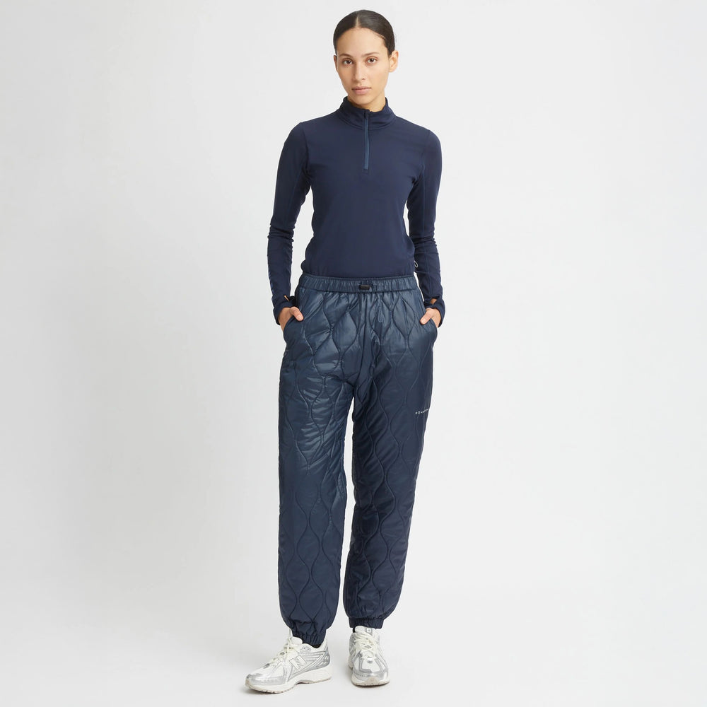 Against a plain background, a person wears Rohnisch Relaxed Quilt Pants and a dark long-sleeve top made from recycled ripstop polyester, paired with sneakers.