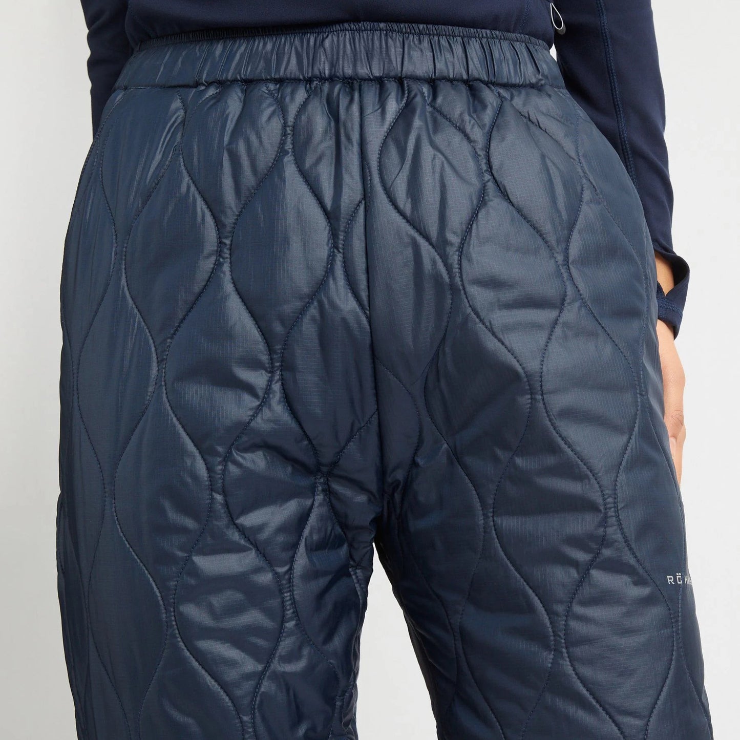 A person is wearing Rohnisch Relaxed Quilt Pants, navy-blue insulating pants made from recycled ripstop polyester with an elastic waistband.