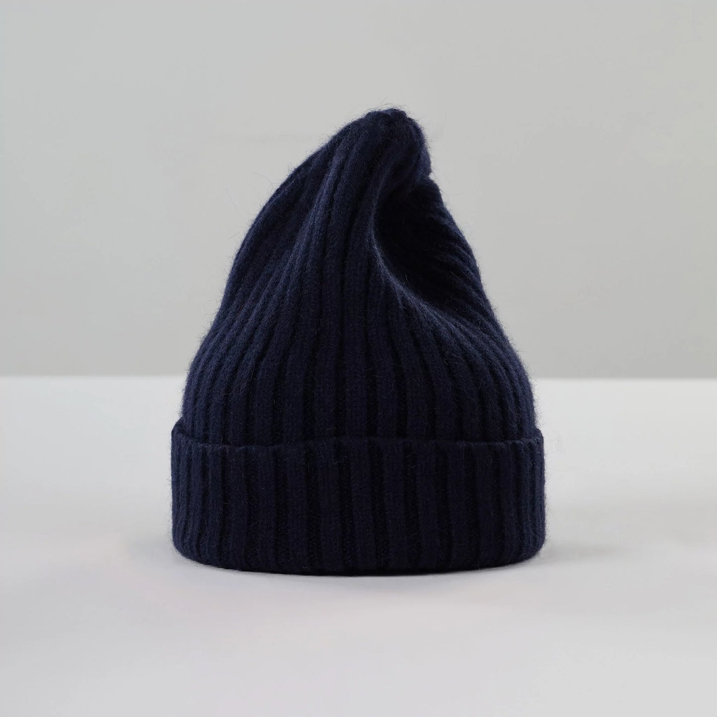 Le Bonnet's Beanie, Midnight, crafted from soft lambswool in dark blue ribbed texture, stands upright on a plain surface.