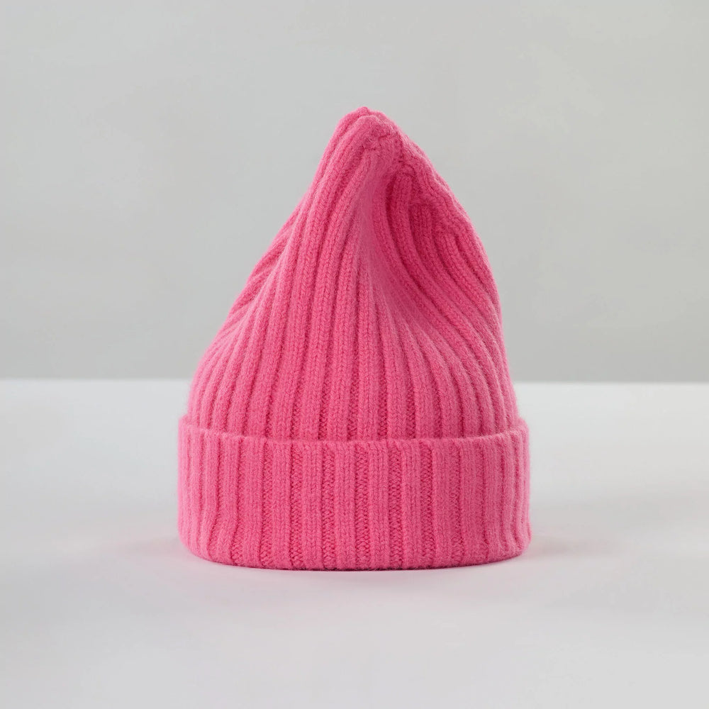 A large, bubblegum pink, ribbed knit beanie by Le Bonnet, designed for extreme comfort with a pointed top, rests on a plain surface.